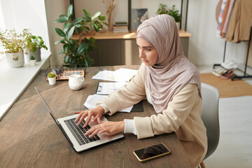 Middle Eastern businesswoman wearing stylish hijab and abaya working on laptop in modern workplace,...