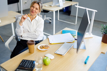 Adult female office worker eating cookies during coffee break