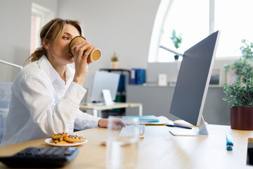 Pretty business woman drinking coffee while working at the computer in the office