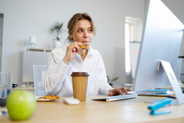 Hungry businesswoman office worker snacking on cookies while working on computer
