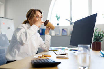 Focused on working at the computer business woman drinking coffee with cookies indoor