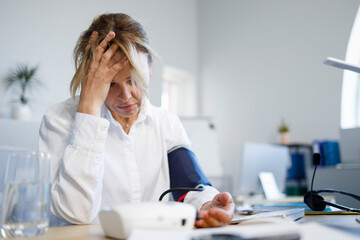 Stressed business woman measuring her blood pressure while sitting at workplace