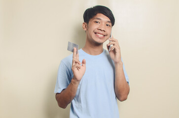 Portrait of happy asian young man holding smart phone and ATM card, isolated background