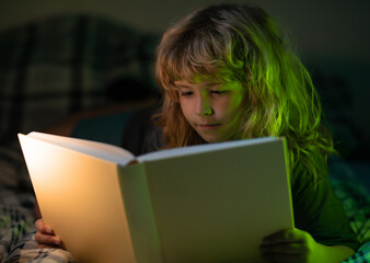 Child read fairy tale from book. Child little boy reading a book in the dark home. Kids face with...