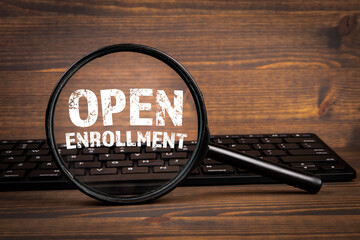 Open Enrollment. Search, Research and Registration concept. Magnifying glass and computer keyboard on a wooden background
