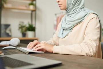 Head cropped shot of serious Muslim female freelancer sitting at table working on computer at home