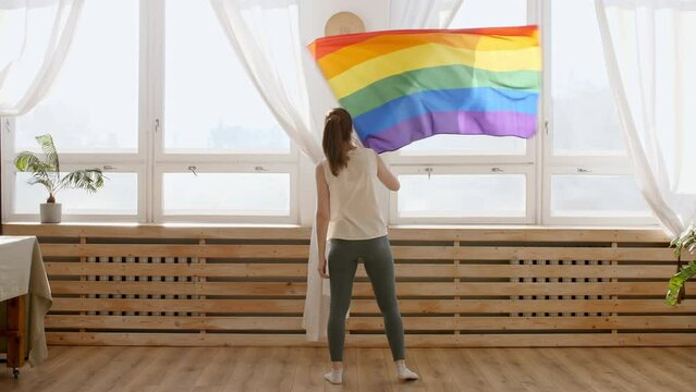 Female holding LGBT gay flag in hands and waving on sunset in sunny rays. Rainbow LGBT flag - Lesbian, gay, bisexual, transgender social movements. High quality 4k footage