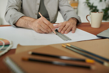 Close-up of unrecognizable engineer sitting at table and drawing line using ruler while working with technical plan