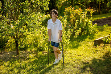 Cute child, boy, walking with crutches in a garden