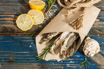 Sun-dried smelt in a paper package. Salted fish with marine decor. Lemon, fresh rosemary, sea rope