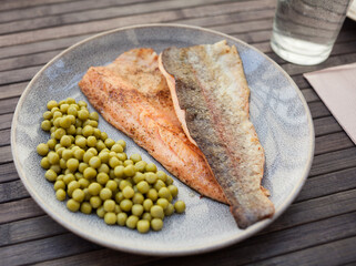 Top view of baked trout fillet served on plate with peas closeup