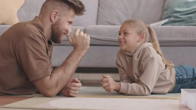 Slowmo of modern father arm wrestling with his little daughter and letting her to win, lying on rug in living room