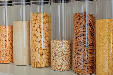 Shelf in the kitchen with stocks of cereals and pasta: oatmeal, peas, rice, pasta in glass jars. Order in the kitchen