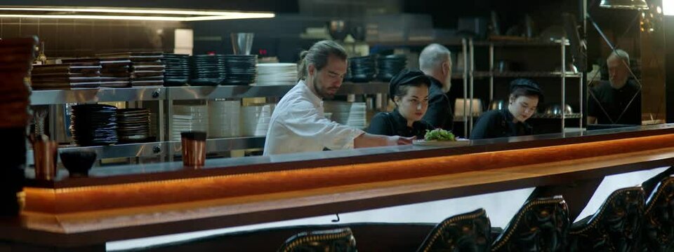WIDE Caucasian male chef working on modern busy commercial restaurant kitchen. Shot with 2x anamorphic lens