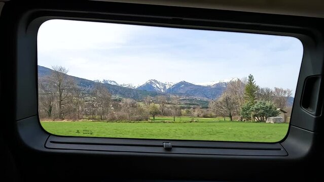 Vue &agrave; travers la fen&ecirc;tre depuis l'int&eacute;rieur d'un van am&eacute;nag&eacute; avec vue sur la prairie et l'herbe, les arbres et les montagnes