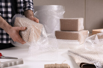 Man covering box with bubble wrap at table in warehouse, closeup