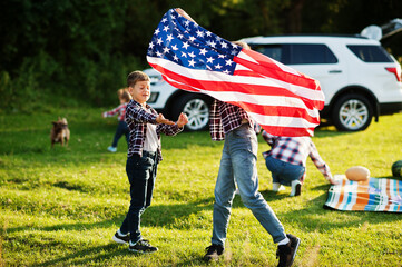 American family spending time together. Brothers play with USA flags against big suv car outdoor....
