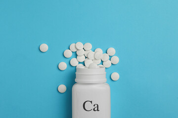 Fototapeta na wymiar Overturned bottle of calcium supplement pills on light blue background, flat lay