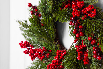 Fototapeta na wymiar Beautiful Christmas wreath with red berries hanging on white door, closeup