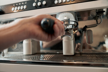 Close-up photo of hands of male barista installing filter with pressed coffee into coffee machine