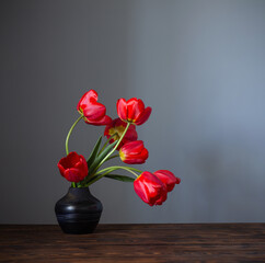 red tulips in dark ceramic vase on wooden table