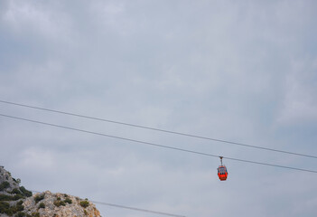 Red cabins of funicular in Antalya, Turkey against backdrop of rain clouds. Cable car trip to viewpoints in mountains. During trip by cable car Tourists enjoy beautiful views of city and nature