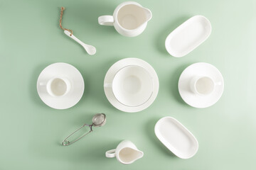 white ceramic and porcelain cups, saucers, milk jug of different shapes on a light green background. top view. flat lay.