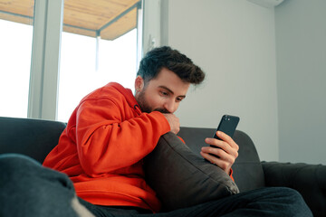 Young male on sofa look at smartphone screen texting or messaging online or watching video....