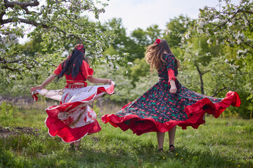 two dancers in traditional gypsy dresses dance in nature on a spring day - obrazy, fototapety, plakaty