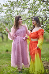 Beautiful women enjoying the garden with flowering trees, young women with flowers in the green park. cheerful teenagers walking outdoors. soft light style color