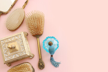 Image of vintage hair comb, perfume bottle and hand mirror over pastel pink background