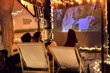 Fotobehang Young cheerful people watching a movie on camping site © gpointstudio