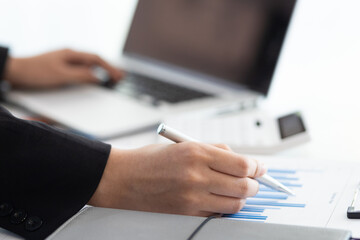 Businesswoman finance market analyst working on laptop pointing at business finance report chart document on desk in office. Financial planning and accounting concepts.