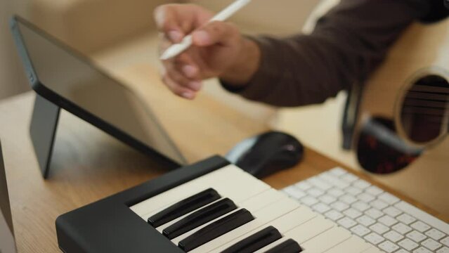Close up hand Professional songwriter playing guitar and piano keyboard with tablet for Mixing and Mastering music. Male composing a song with audio equipment at Recording studio. Musician concept