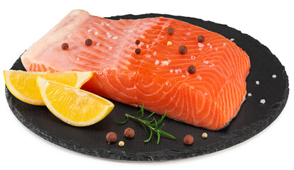 Red fish. Raw salmon fillet with rosemary, peppercorns and lemon on black round stone plate isolate...