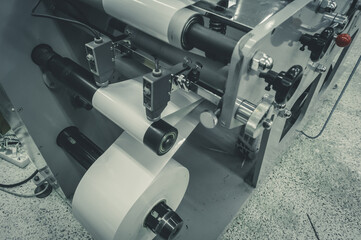 Roller of white printing paper for self-adhesive label on the shaft of the die-cutting machine in the printing house. Selective focus