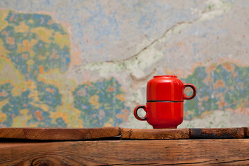 Two ceramic small red espresso cups, standing on a wooden table. A colorful old wall in the...