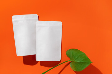 White cardboard packaging for tea/coffee/spices/snack and monstera leaf on orange background. Branding and packaging mockup.
