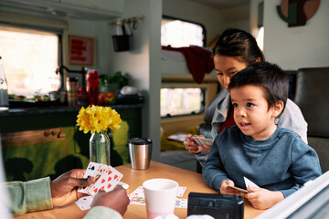 An interracial family sits in their motor home and plays cards.