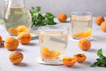Homemade apricot compote in two glasses and jug on light gray background
