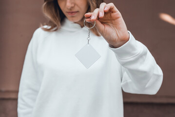 White rhombus keychain mockup in woman's hand. Blank white sublimation keychain. - obrazy, fototapety, plakaty