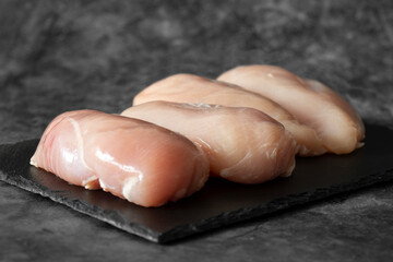 Raw chicken breast fillets on a slate cutting board.  On a dark stone background