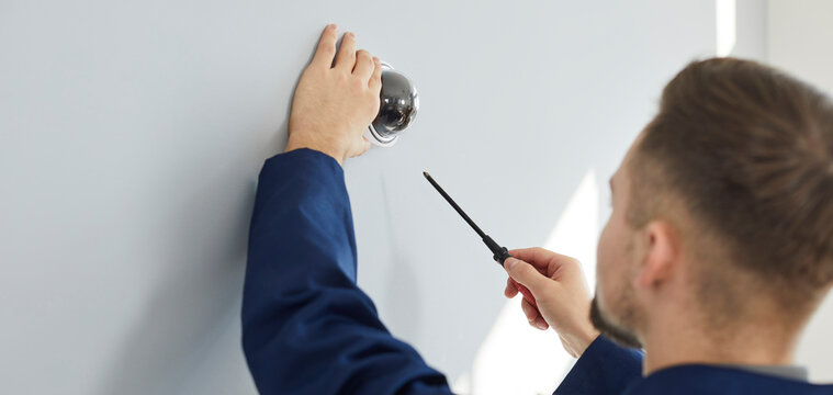 Electrician installing security camera for theft deterrence in building. Repair service worker using screwdriver to fit screws and adjust wall mounted CCTV surveillance dome cam at home or in office