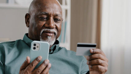 Elderly African Dominican old mature man at home online transaction buying hold smartphone credit...