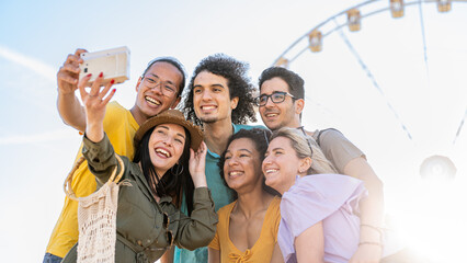 Group of six people having fun taking photos with vintage camera, influeancers of generation z creating contents for social media, farris wheel on background