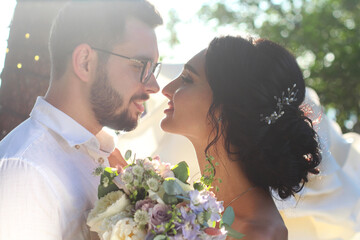 An incredibly beautiful brunette and a bearded guy in glasses kiss at sunset on their wedding day. Two lovers on a romantic date. Love background concept