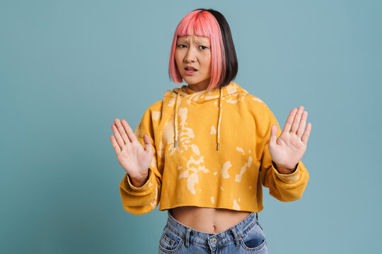 Asian girl with pink hair and piercing showing stop gesture at camera