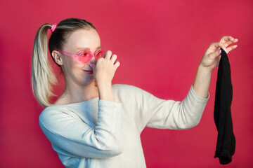 a beautiful girl in pink glasses on a pink background with surprise and disgust holds a dirty black...