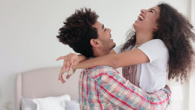 Young couple in love is hugging and showing house keys to camera in modern apartment spbi. 4k Close view of happy curly people hug tenderly and talk with smiles, hold keys in hands and stand in light