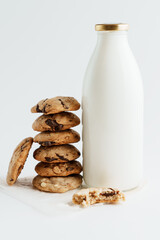 A pile of homemade cookies with pieces of chocolate next to a bottle of milk